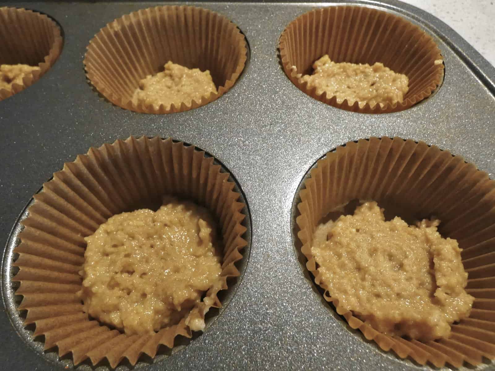 Thin layer of orange cranberry batter in muffin cups