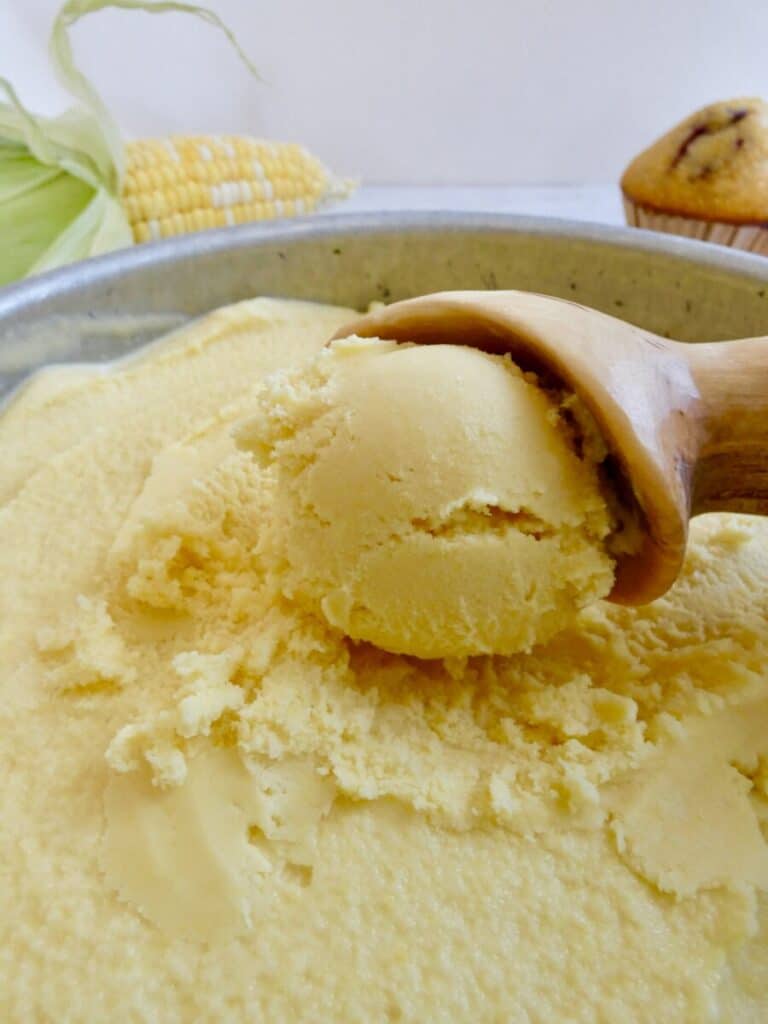 sweet corn ice cream being scooped out of an ice cream container with corn and cornbread muffin in the background