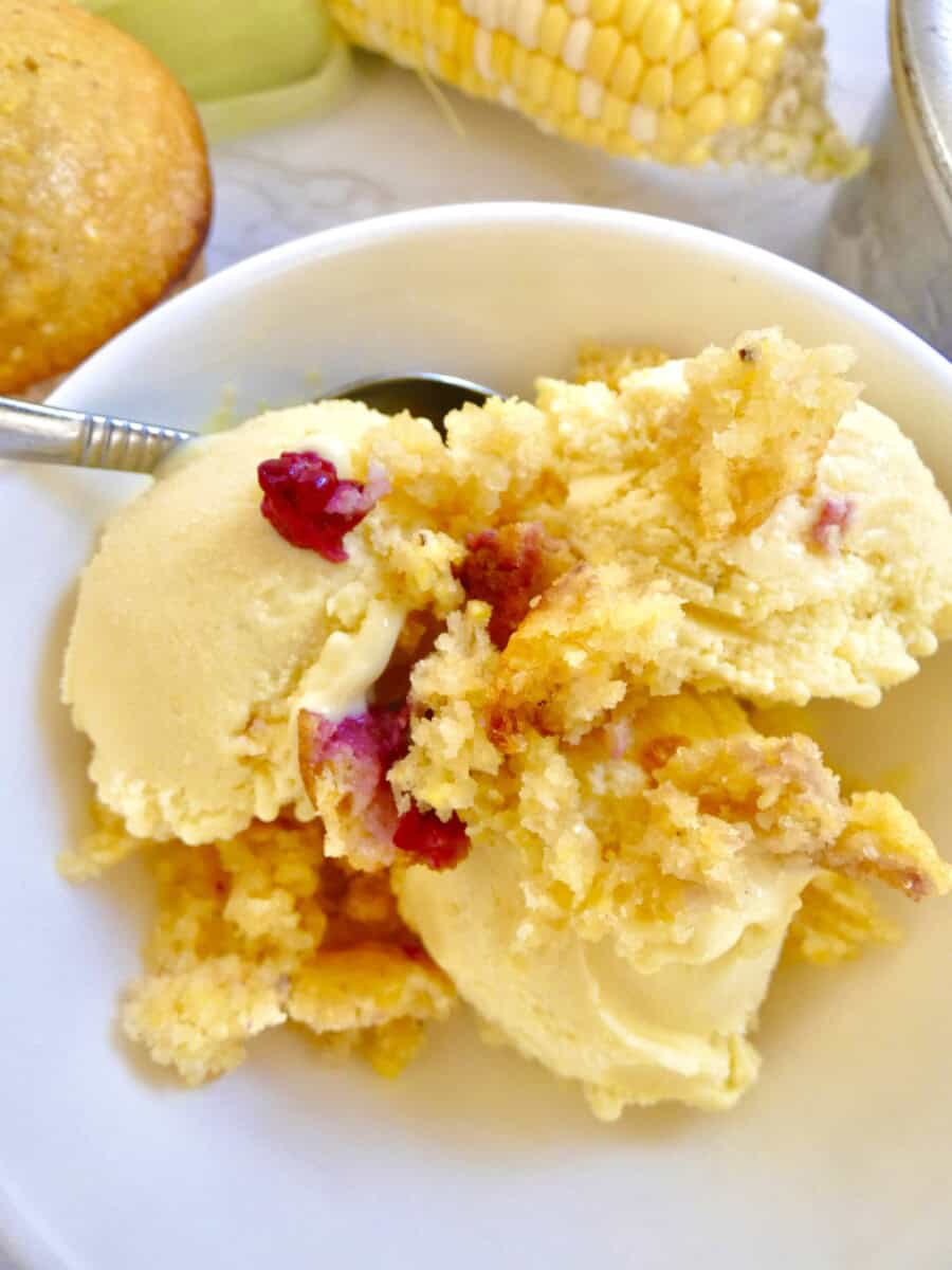 bowl of sweet corn ice cream topped with cornbread with fresh corn in the background