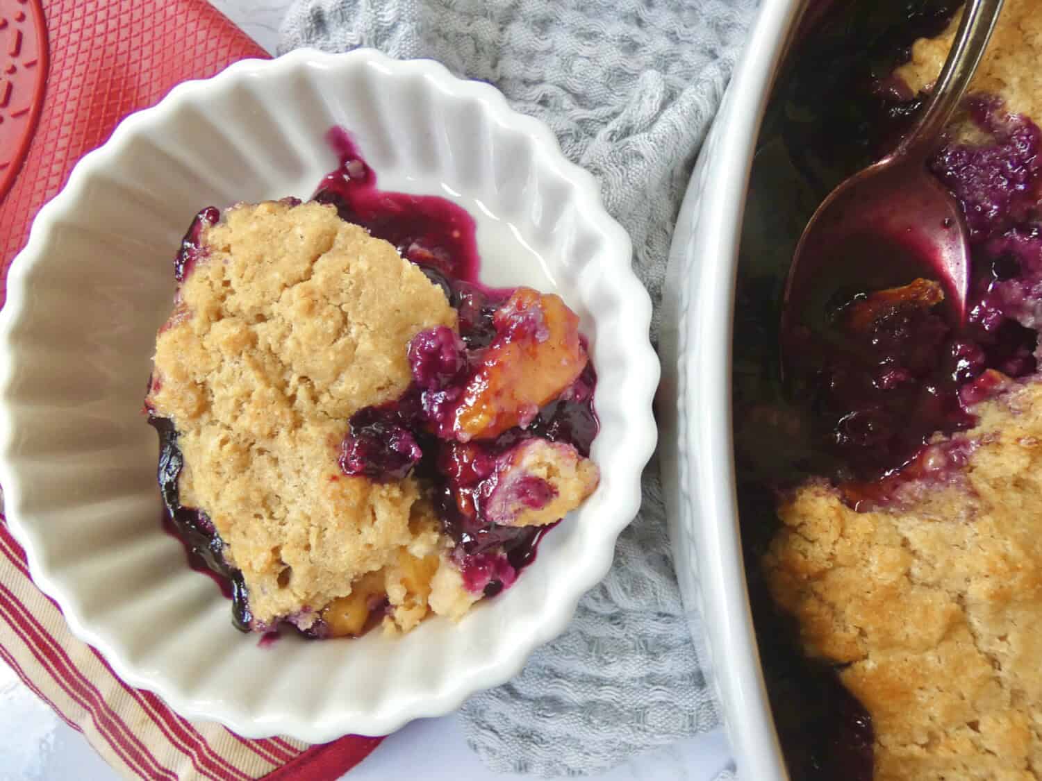 bowl of healthier blueberry peach cobbler with baking dish