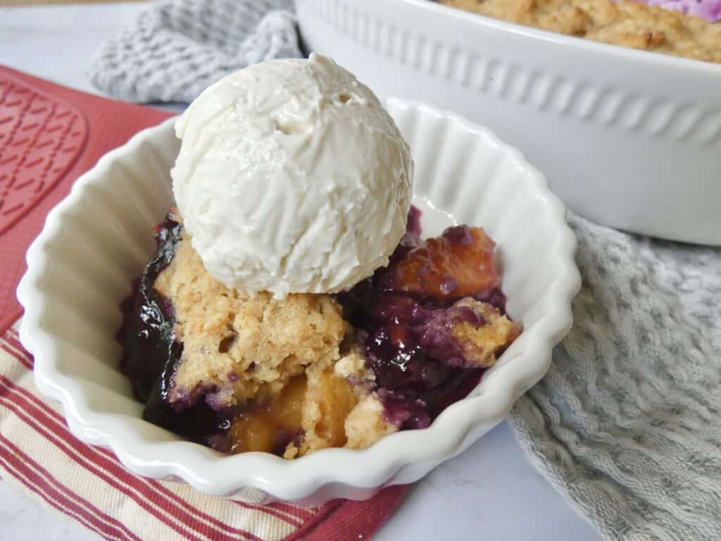 bowl of healthier blueberry peach cobbler with scoop of vanilla ice cream