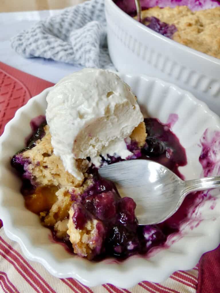 bowl of healthier blueberry peach cobbler with vanilla ice cream and spoon