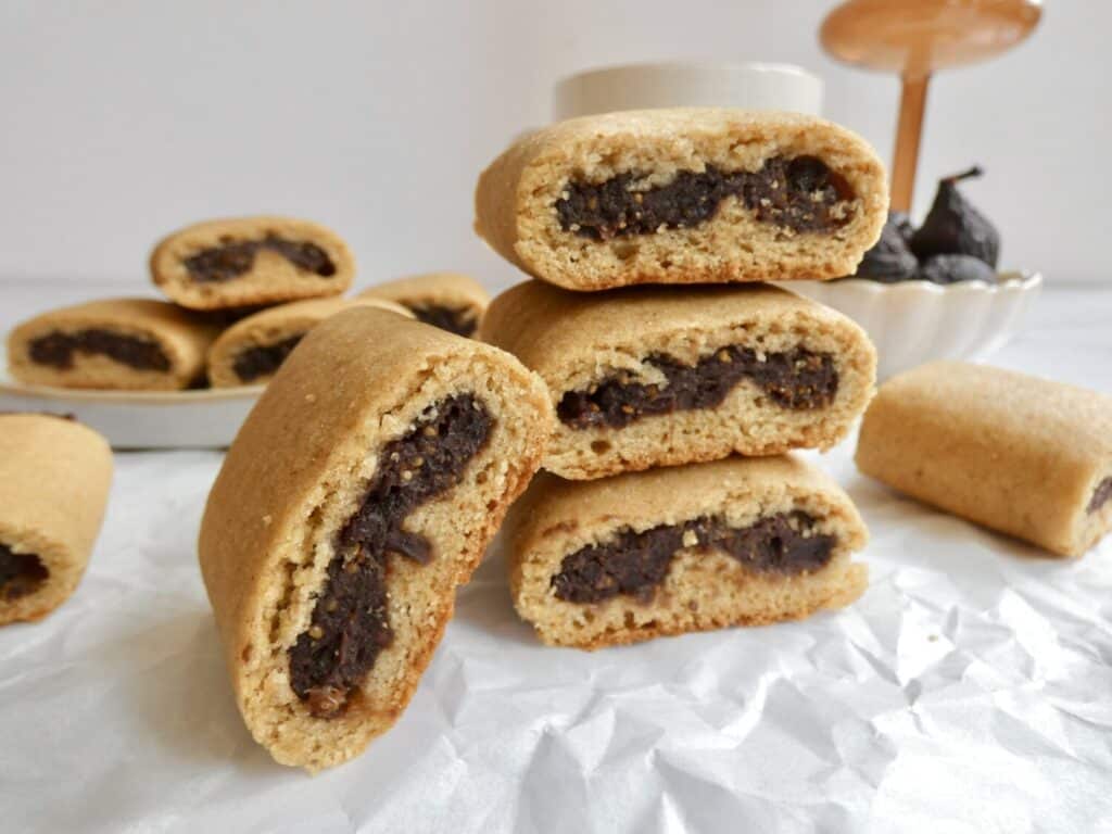 stack of Healthy Homemade Fig Newtons on parchment paper with a bowl of figs in the background