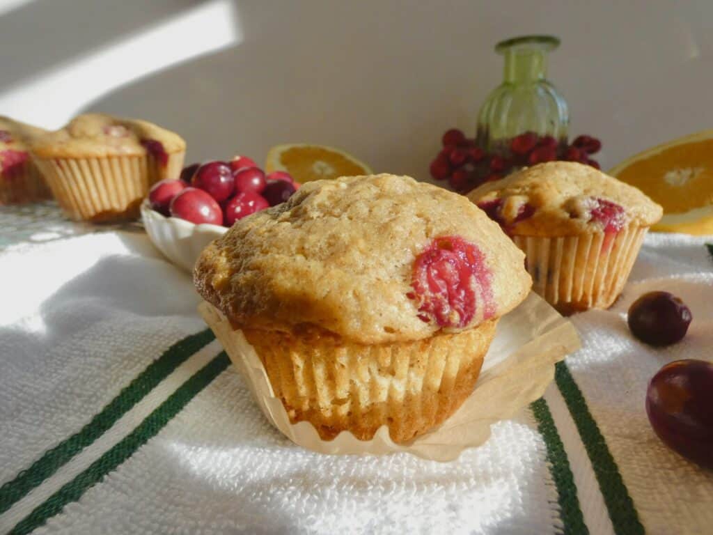 cranberry orange muffin sitting on top of a paper liner with fresh cranberries in the background