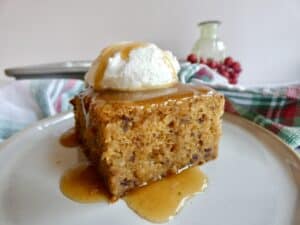 slice of Healthier Sticky Toffee Pudding Cake on a plate with cream and toffee sauce