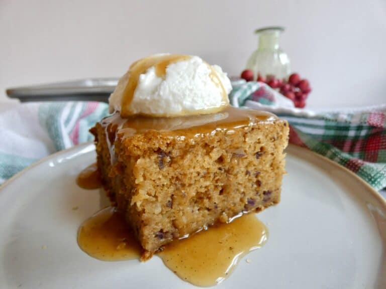 slice of Healthier Sticky Toffee Pudding Cake on a plate with cream and toffee sauce